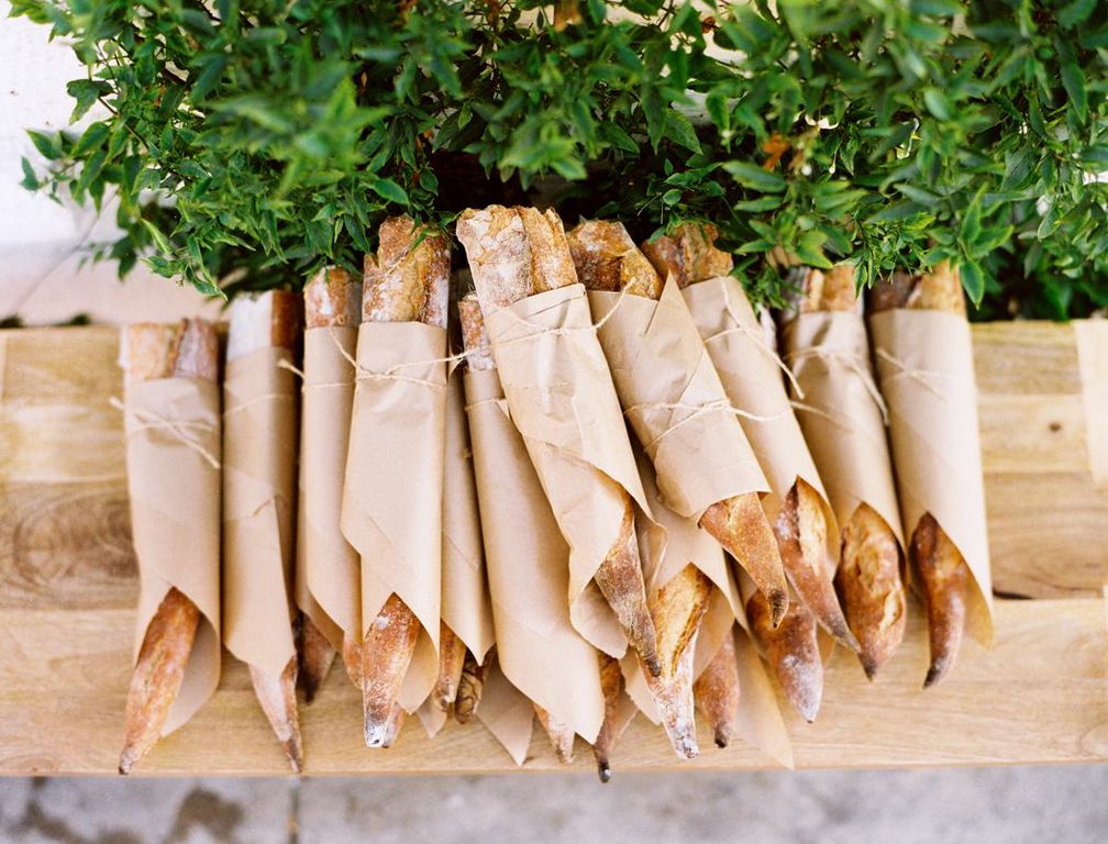 Baguettes wrapped in paper lined up on a wooden board