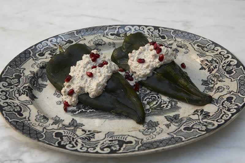 Chiles en nogada topped with walnut sauce and pomegranate seeds on a patterned plate