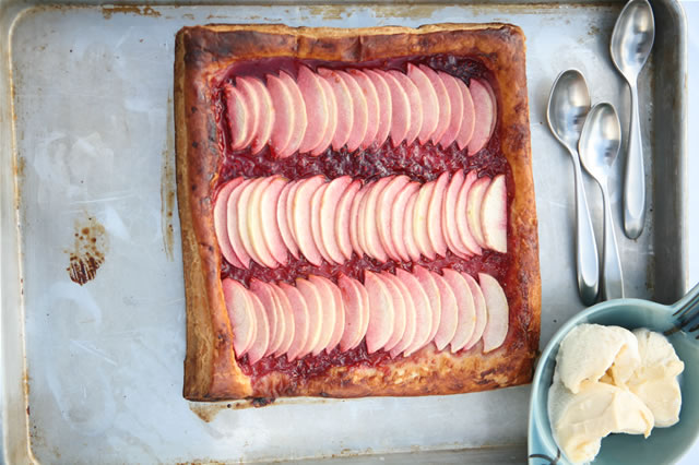 A free-form fruit tart on a baking sheet beside silver spoons