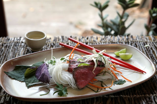 Rice noodles with grilled beef, herbs and chopsticks on a woven tray